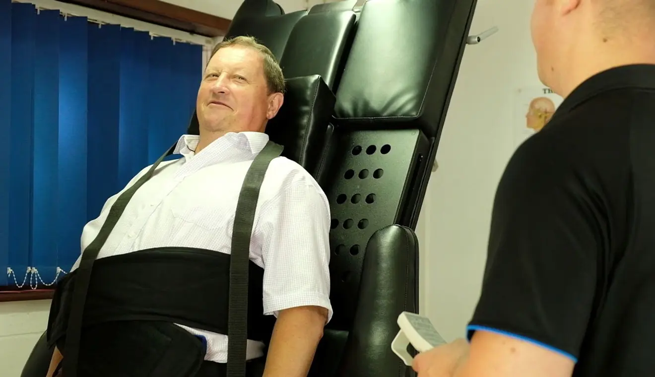 A patient harnessed into the Accu SPINA IDD Therapy machine while a clinician sets up the treatment